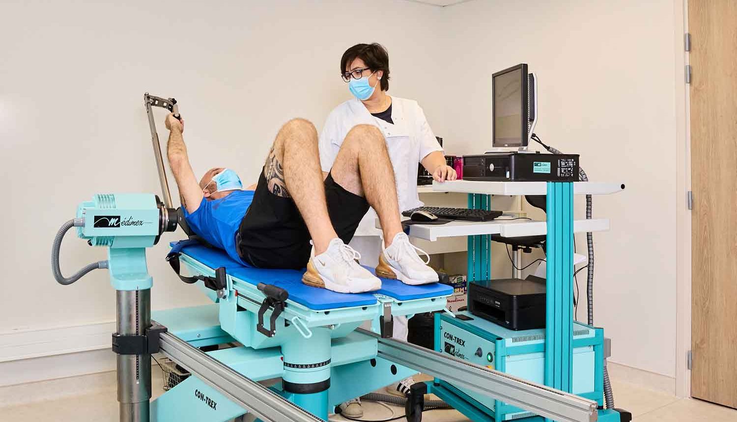 Infirmière débout guidant son patient en tenue de sport allongé sur une machine médicale